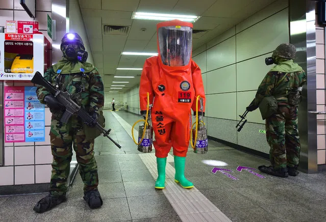A rescue member (C) in full protective gear stands amongst South Korean soldiers wearing gas masks during an anti-terror drill on the sidelines of South Korea-US joint military exercise, called Ulchi Freedom, at a subway station in Seoul on August 23, 2016. South Korea and the United States kicked off large-scale military exercises on August 22, triggering condemnation and threats of a pre-emptive nuclear strike from North Korea. (Photo by Jung Yeon-Je/AFP Photo)
