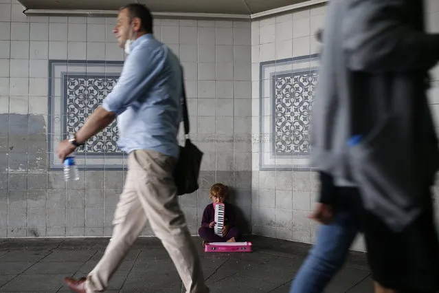 People, some wearing protective masks against the spread of coronavirus, walk by a child playing music for money on an underpass in Istanbul, Thursday, June 18, 2020. (Photo by Emrah Gurel/AP Photo)