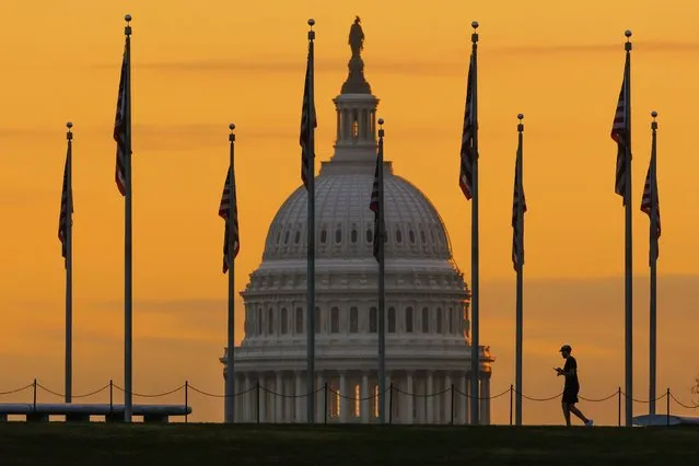 An early morning pedestrian is silhouetted against sunrise as he walks through the U.S. Flags on the National Mall and past the US Capitol Building in Washington Monday, November 7, 2022, one day before the midterm election will determine the control of the US Congress. (Photo by J. David Ake/AP Photo)