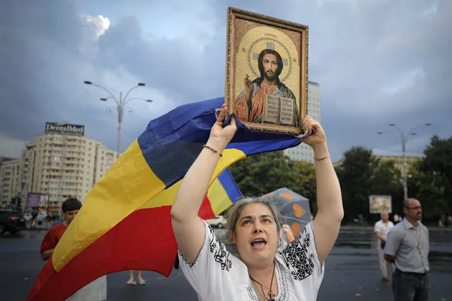 A woman shouts slogans holding a flag and a religious icon during a protest outside the government headquarters against recently passed legislation that enables authorities to impose quarantine or isolation measures on COVID-19 infected people in Bucharest, Romania,Sunday, July 19, 2020. Over the past week Romania has registered the highest number of COVID-19 infection cases since the pandemic reached the country in February, with up to 889 in a 24 hours interval, as many fail to observe the mandatory protection measures, like the use of a face mask indoors and on public transport or maintaining social distancing. (Photo by Vadim Ghirda/AP Photo)