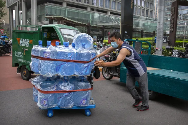 A worker wearing a face mask to protect against the coronavirus pushes a cart loaded with bottles of drinking water in Beijing, Friday, July 17, 2020. Further restrictions are being imposed on the northwestern Chinese city of Urumqi following a cluster of new cases. (Photo by Mark Schiefelbein/AP Photo)