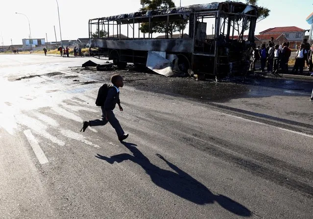 A child runs near a bus which was set alight during a two day strike by taxi operators over a number of grievances against traffic authorities in Cape Town, South Africa on November 21, 2022. (Photo by Esa Alexander/Reuters)