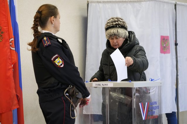A woman casts a ballot as a police officer guards at a polling station during the presidential election in St. Petersburg, Russia, Sunday, March 17, 2024. Voters in Russia are going to the polls for the last day of a presidential election that is all but certain to extend President Vladimir Putin's rule after he clamped down on dissent. (Photo by Dmitri Lovetsky/AP Photo)