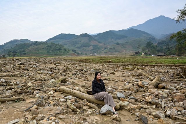 This photo taken on March 20, 2025 shows Nguyen Thi Kim sitting on a pillar of a destroyed house at the original site of Lang Nu village in Lao Cai province, after part of it was wiped away in a landslide triggered by Typhoon Yagi's devastating heavy rains last year. Dozens of survivors have been relocated to a site that authorities hope will withstand future climate change-linked disasters, with stronger homes, drainage canals and a gentler topography that lessens landslide risks. (Photo by Nhac Nguyen/AFP Photo)