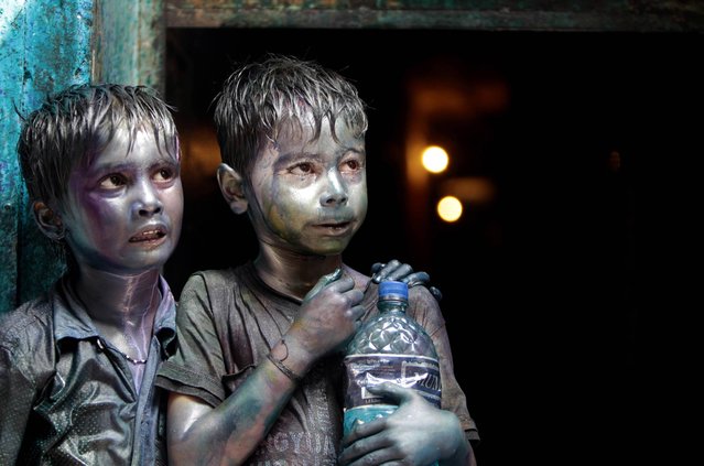Bangladeshi Hindu children smeared in colors stand at a doorway as they watch Holi festival celebrations in Dhaka, Bangladesh, Thursday, March 28, 2013. Hindus celebrate Holi, the festival of colors, by painting each other in bright pigments, distributing sweets and squirting water at one another. The holiday celebrated mainly in India and Nepal marks the beginning of spring and the triumph of good over evil. (Photo by A.M. Ahad/AP Photo)