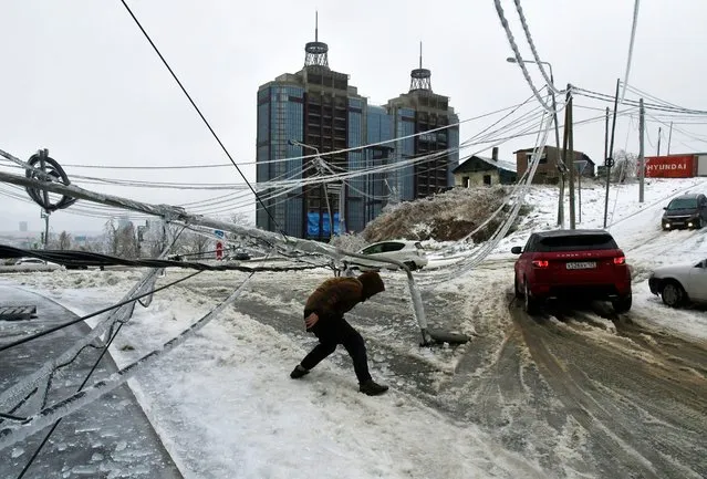 A man walks under a damaged power pole covered with ice after freezing rain in the far eastern city of Vladivostok, Russia on November 19, 2020. (Photo by Yuri Maltsev/Reuters)
