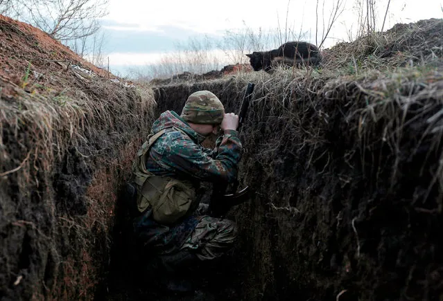 A cat looks down at a Ukrainian soldier resting in a trench on the front line with Russia backed separatists near Krasnogorivka village, Donetsk region on February 28, 2020. Two Ukrainian soldiers were killed on March 10, 2020, and nine others wounded in fighting with pro-Russian separatists in the east of the country, the second “escalation” of the conflict in recent weeks. (Photo by Anatolii Stepanov/AFP Photo)
