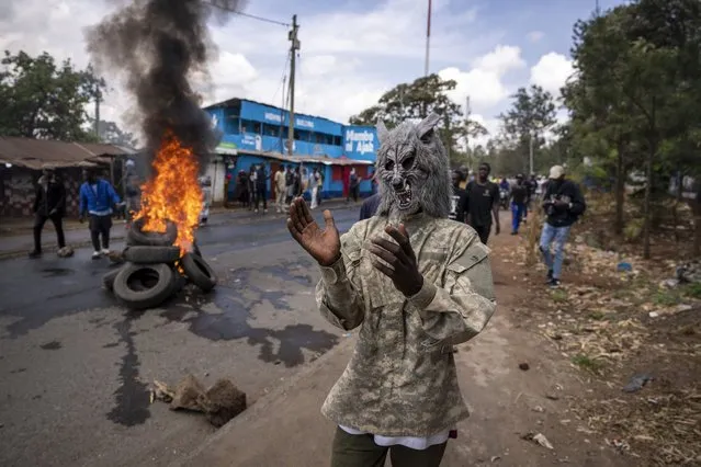 A protester wearing a wolf mask stands next to a burning barricade in the Kibera slum of Nairobi, Kenya Monday, March 20, 2023. (Photo by Ben Curtis/AP Photo)
