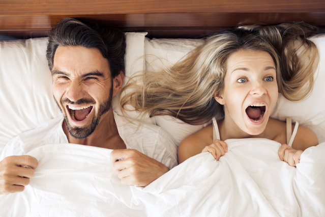 Top view of beautiful young woman and her man showing surprise and looking at camera while lying in bed under blanket. (Photo by Yuriy Zhuravov/Shutterstock)