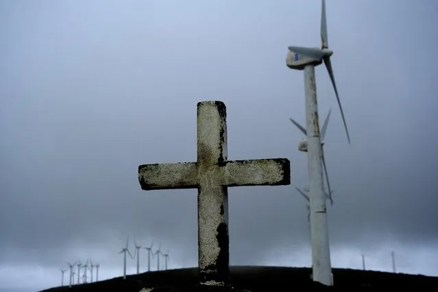 A cross is pictured in front of wind turbines surrounded by fog at a wind farm in the Serra da Capelada, near Ferrol, Galicia, Spain on April 13, 2023. (Photo by Nacho Doce/Reuters)