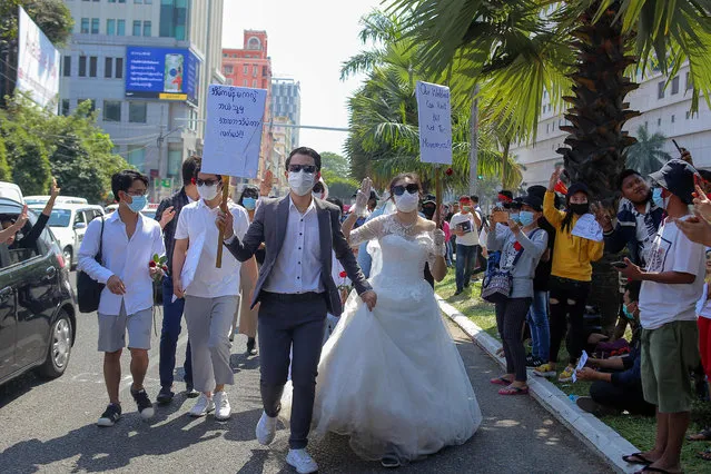 Protesters wearing wedding attire and carrying signs – on (L) translates as “Except my wife at home, I accept nobody's coup!” and on (R) that reads “Our wedding can wait but not this movement!” – take part in a demonstration against the military coup in Yangon on February 9, 2021. (Photo by AFP Photo/Stringer)