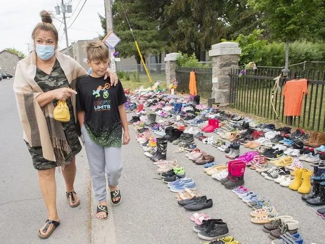 Lynn Karonhia-Beauvais and grandson Jamieson Kane walk past shoes representing the remains of 215 children outside St. Francis Xavier Church in Kahnawake, Quebec, Sunday, May 30, 2021. The remains of 215 children, some as young as 3 years old, have been found buried on the site of what was once Canada's largest Indigenous residential school – one of the institutions that held children taken from families across the nation. (Photo by Graham Hughes/The Canadian Press via AP Photo)