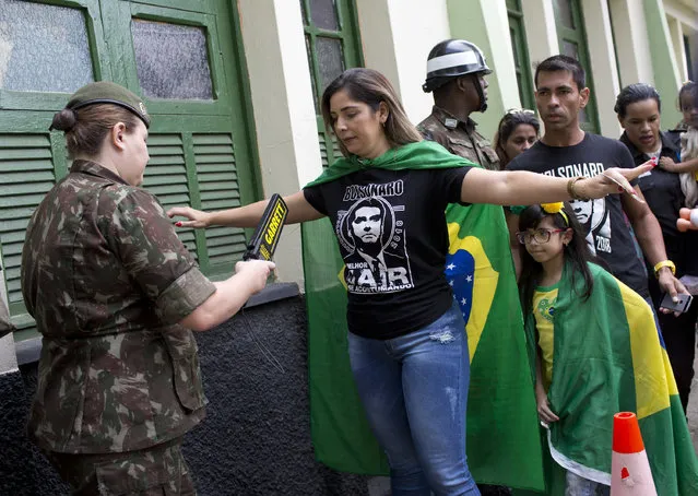 A supporter wearing a T-shirt of Jair Bolsonaro, presidential candidate with the Social Liberal Party, is checked by an army police at a polling station in Rio de Janeiro, Brazil, Sunday, October 28, 2018. (Photo by Silvia Izquierdo/AP Photo)