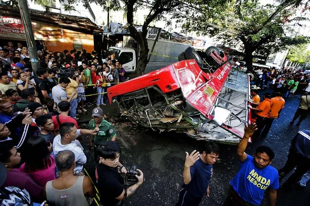 People gather at the scene where a passenger bus plunged from an elevated highway known as the Skyway, in suburban Paranaque, southeast of Manila, Philippines, on December 16, 2013. Officials said at least 21 people died, mostly passengers, and more than 20 others  were injured in the accident. (Photo by Bullit Marquez/Associated Press)