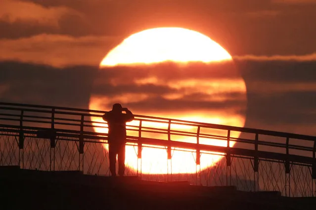 A man on a bridge takes photograph of the first sunrise of the year at a park in Seoul, South Korea on January 1, 2024. (Photo by Kim Hong-Ji/Reuters)