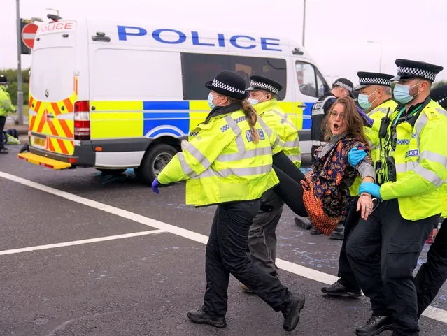 Police officers carry away a protester who had glued herself to a slip road at Junction 4 of the A1(M), near Hatfield, England, Monday September 20, 2021. Environmental activists who have repeatedly blocked Britain’s busiest highway face possible imprisonment after a judge granted an injunction against the protesters, Britain’s transport secretary said Wednesday Sept. 22, 2021. (Photo by Steve Parsons/PA Wire via AP Photo)