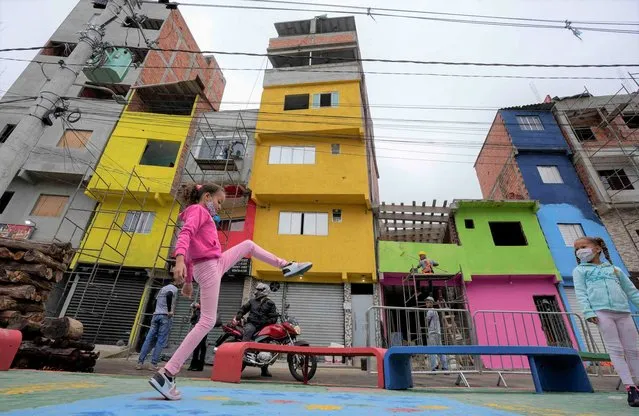 Workers paint the facades of residences in the Paraisopolis favela, as a child plays in the foreground during the community's centennial celebration, in Sao Paulo, Brazil, Thursday, September 16, 2021. One of the largest favela's in Brazil, home to tens of thousands of residents in the country's largest and wealthiest city, Paraisopolis is grappling with crime and a pandemic that have challenged daily life for many who live there, but organizers say its people have built a vibrant community and are launching a 10-day celebration of its achievements. (Photo by Andre Penner/AP Photo)