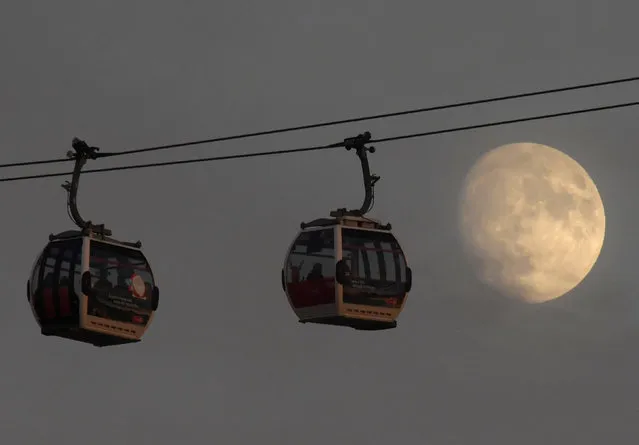 Passengers cross the River Thames in cable cars with the moon seen behind at Greenwich Peninsula in London, Britain December 11, 2016. (Photo by Toby Melville/Reuters)