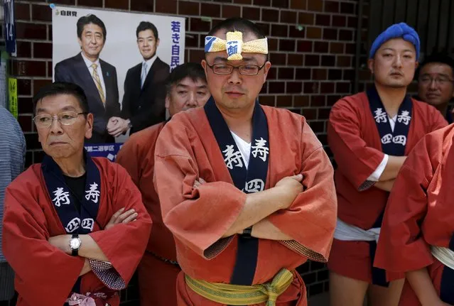 Revellers stand in front of an election poster showing Japanese Prime Minister Shinzo Abe (back L) as they watch a portable shrine paraded through a street during the Sanja Matsuri festival in the Asakusa district of Tokyo May 17, 2015. (Photo by Thomas Peter/Reuters)