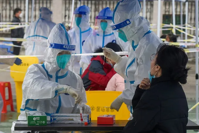 Medical workers in protective suits collect swabs from residents at a nucleic acid testing site during a third round of mass testing for the coronavirus disease (COVID-19) in Zhenhai district of Ningbo, Zhejiang province, China on December 12, 2021. (Photo by Cnsphoto via Reuters)