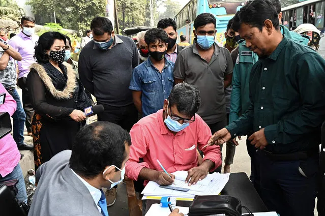 A commuter (R) pays a fine to a magistrate after being stopped and fined by policemen while outdoors without a facemask, along a street in a mobile court in Dhaka on January 13, 2022. (Photo by Munir Uz Zaman/AFP Photo)