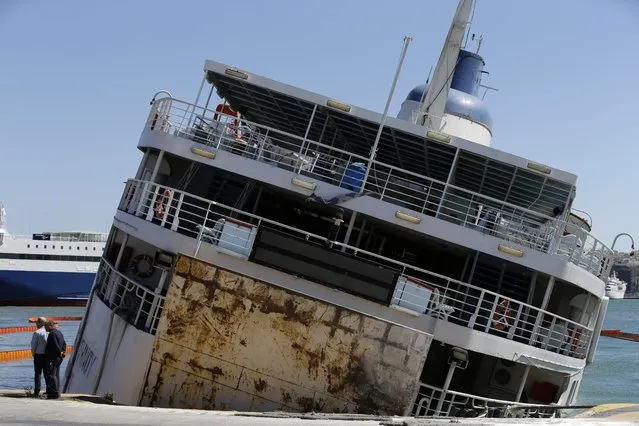 Dockworkers check an old, out-of-service ferry boat that has listed sharply to starboard at its moorings in Greece's main port of Piraeus, near Athens, on Tuesday, April 26, 2016. The Panaghia Tinou took in water for unknown reasons Tuesday and a floating boom was set up around it to prevent pollution from its tanks. No injuries were reported. (Photo by Thanassis Stavrakis/AP Photo)
