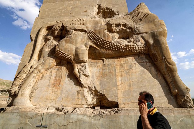 A man speaks on a cell phone while walking past a relief on an ancient gate in the ruins of ancient Persepolis, which served as the capital of the Achaemenid Persian Empire (550-330 BC), in southern Iran on May 13, 2024. (Photo by Atta Kenare/AFP Photo)