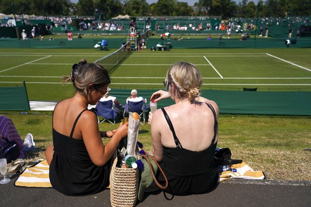 Spectators have a drink as they sit on the grass at the Roehampton Community Sports Centre in Roehampton, London, Wednesday, June 26, 2024, during Wimbledon qualifying. (Photo by Alberto Pezzali/AP Photo)