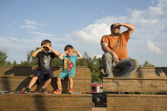 In this July 17, 2015 photo, Tony Breeden and his two sons Landon, left, and Logan, shield their eyes from the late afternoon sun and the gritty air while watching dirt track racing at the Ponderosa Speedway in Junction City, Ky. The boys were watching their cousin race. (Photo by David Stephenson/AP Photo)