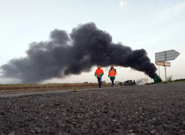 Two union activists in fluorescent vests walk toward the Normandie Bridge outside of Le Havre, western France, during a blockade action, Thursday, May 26, 2016. The cloud of black smoke is from burning tires. French Prime Minister Manuel Valls says he is open to “improvements and modifications” in a labor bill that has sparked intensifying strikes and protests, but will not abandon it. (Photo by Raphael Satter/AP Photo)
