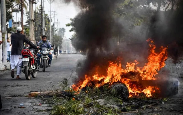 Commuters pass by a fire on a road set by demonstrators during a protest against the government's Citizenship Amendment Bill (CAB) in Guwahati on December 12, 2019. Indian police fired blanks on December 12 as thousands of protesters ignored a curfew in the north-east of the country, in a fresh day of demonstrations against contentious new citizenship legislation. (Photo by Biju Boro/AFP Photo)