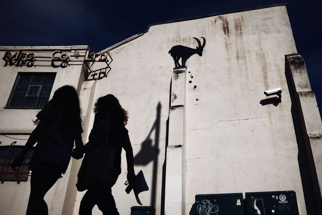 A photograph taken on August 5, 2024 shows people walking past a stencilled Banksy artwork, depicting a mountain goat and falling rubble at the top of a pillar, on the side of a building in Kew Gardens, west London. The artist confirmed the work to be theirs after posting an image of it on the social media app Instagram. (Photo by Benjamin Cremel/AFP Photo)