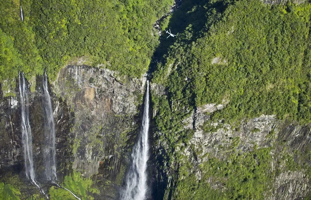 A helicopter passes over a waterfall on the forested lower slopes of the Piton de la Fournaise “Peak of the Furnace” volcano, on the southeastern corner of the Indian Ocean island of Reunion Saturday, August 1, 2015. (Photo by Ben Curtis/AP Photo)