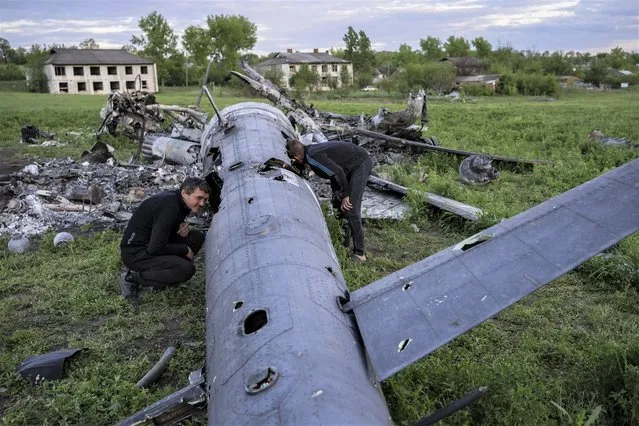 Oleksiy Polyakov, right, and Roman Voitko check the remains of a destroyed Russian helicopter lie in a field in the village of Malaya Rohan, Kharkiv region, Ukraine, Monday, May 16, 2022. (Photo by Bernat Armangue/AP Photo)