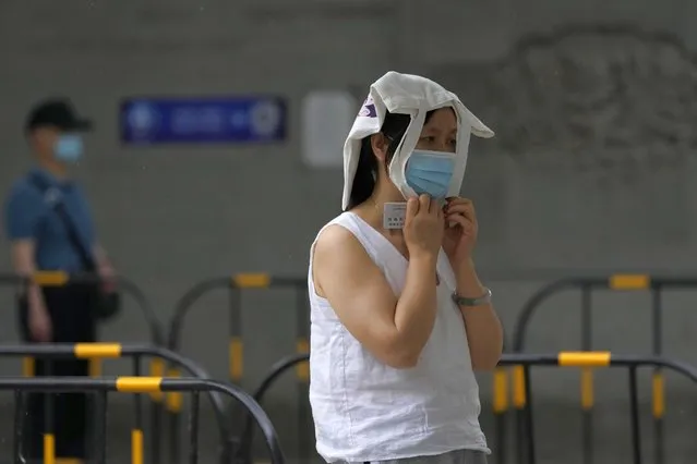 A resident covers her head as it starts to rain at a mass COVID test site, Sunday, May 29, 2022, in Beijing. (Photo by Ng Han Guan/AP Photo)