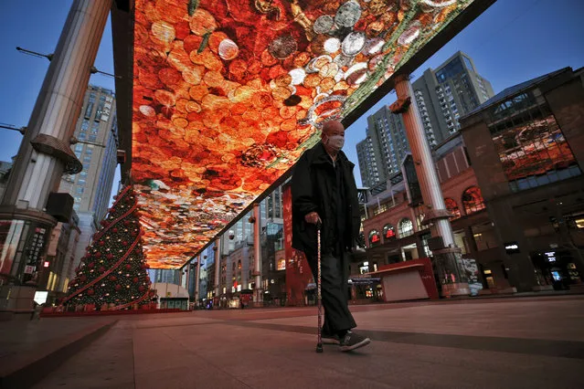 A man walks with a stick passes by a huge screen showing a colourful art at a quiet shopping mall in Beijing, Tuesday, March 10, 2020. China's president Xi Jinping visited the center of the global virus outbreak Tuesday as Italy began a sweeping nationwide travel ban and people worldwide braced for the possibility of recession. For most people, the new coronavirus causes only mild or moderate symptoms, such as fever and cough. For some, especially older adults and people with existing health problems, it can cause more severe illness, including pneumonia. (Photo by Andy Wong/AP Photo)