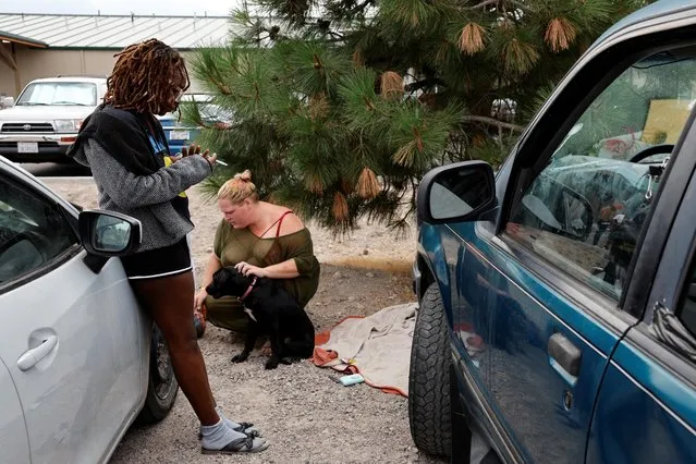 Paisley Bamberg, Kylie Hughes and their dog Selenith from Yreka, who have evacuated the area amidst the fast-moving McKinney Fire, stand near some cars outside an evacuation shelter in Weed, California, U.S. July 31, 2022. (Photo by Fred Greaves/Reuters)