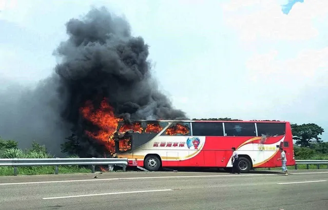 In this photo provided by Yan Cheng, a policeman and another man try to break the windows of a burning tour bus on the side of a highway in Taoyuan, Taiwan, Tuesday, July 19, 2016. The tour bus carrying visitors from China burst into flames on a busy highway near Taiwan's capital on Tuesday, burning to death over 20 people on board, officials said. (Photo by Yan Cheng/Scoop Commune via AP Photo)