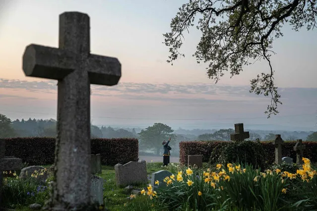 Priest-in-Charge Angie Smith, uses her smartphone to live-broadcast an Easter Sunday service to her congregation at dawn, from the churchyard of Old St. Mary's Church in Hartley Wintney, west of London, on April 12, 2020. Easter events have been cancelled across the country, with the government urging the public to respect lockdown measures by celebrating the holiday in their homes, during the nationwide lockdown to combat the novel coronavirus pandemic. (Photo by Adrian Dennis/AFP Photo)