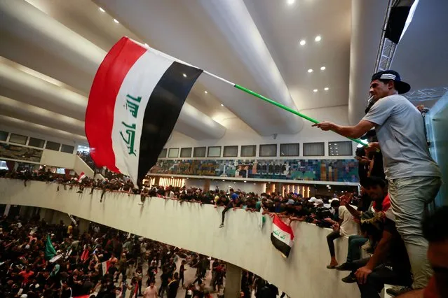 Supporters of cleric Moqtada Sadr wave flags inside Iraq's parliament in the capital Baghdad's high-security Green Zone, as they protest against a rival bloc's nomination for prime minister, on July 30, 2022. The protests are the latest challenge for oil-rich Iraq, which remains mired in a political and a socioeconomic crisis despite elevated global energy prices. Sadr's bloc emerged from elections in October as the biggest parliamentary faction, but was still far short of a majority and, nine months on, deadlock persists over the establishment of a new government. (Photo by Ahmad Al-Rubaye/AFP Photo)