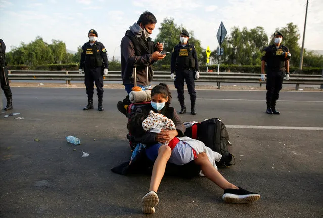 A woman holding a child sits on a motorway surrounded by police while Peruvians who were stranded in Lima during an ongoing quarantine to halt the spread of the coronavirus disease (COVID-19) try to make their way to San Martin and other parts of the country, in Lima, Peru on April 18, 2020. (Photo by Sebastian Castaneda/Reuters)