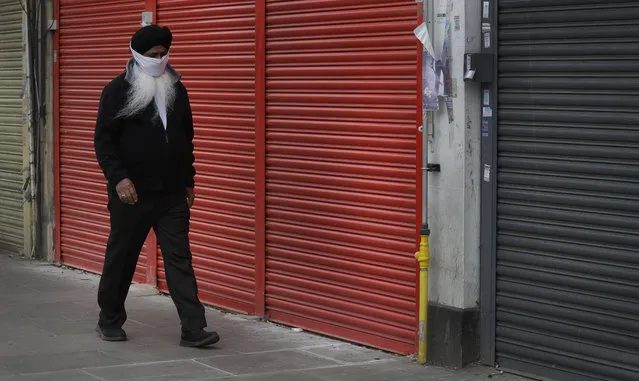 A man wearing a mask to protect against coronavirus, walks past shuttered shops on a usually bustling high street as the country continues its lockdown to help curb the spread of the virus, in London, Monday, April 27, 2020. While Britain is still in lockdown, some nations have begun gradually easing coronavirus lockdowns, each pursuing its own approach but all with a common goal in mind, restarting their economies without triggering a new wave of infections. (Photo by Kirsty Wigglesworth/AP Photo)