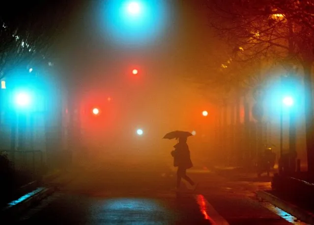A man crosses a street in Frankfurt, Germany, on a rainy and foggy Monday morning, December 27, 2021. (Photo by Michael Probst/AP Photo)