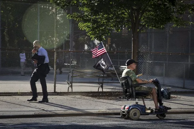A man walks up 2nd Avenue as another rides down on his mobility scooter which flies the U.S. flag in the early morning sunlight, September 16, 2015. (Photo by Carlo Allegri/Reuters)