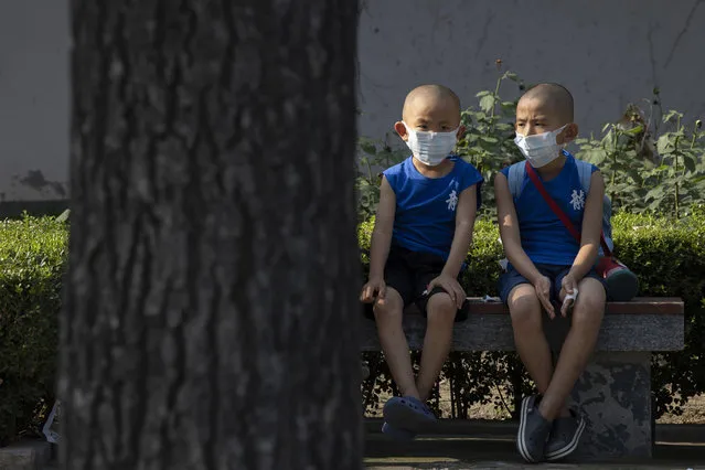 Children wearing masks to curb the spread of the coronavirus sit on a bench in Beijing, China on Monday, July 13, 2020. China reported only a handful of new cases of the virus, all of them brought from outside the country, as domestic community infections fall to near zero. (Photo by Ng Han Guan/AP Photo)