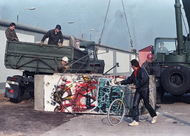 East German workers remove concrete parts of the Berlin Wall and load them onto trucks at the recently opened border crossing point at Potsdam Platz, November 14, 1989. (Photo by Wolfgang Rattay/Reuters)