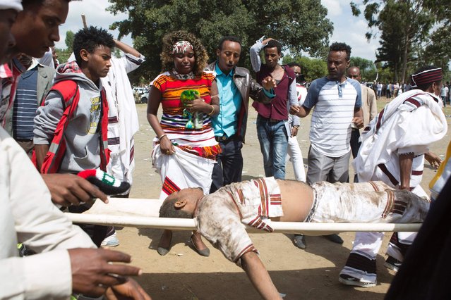 People look at a severely injured man carried for treatment after a deadly stampede in Bishoftu, on October 2, 2016. Several people were killed in a stampede near the Ethiopian capital on October 2 after police fired tear gas at protesters during a religious festival, according to an AFP photographer at the scene. Several thousand people had gathered at a sacred lake to take part in the Irreecha ceremony, in which the Oromo community marks the end of the rainy season, where participants crossed their wrists above their heads, a gesture that has become a symbol of Oromo anti-government protests. The event quickly degenerated, with protesters throwing stones and bottles and security forces responding with baton charges and then tear gas grenades. (Photo by Zacharias Abubeker/AFP Photo)