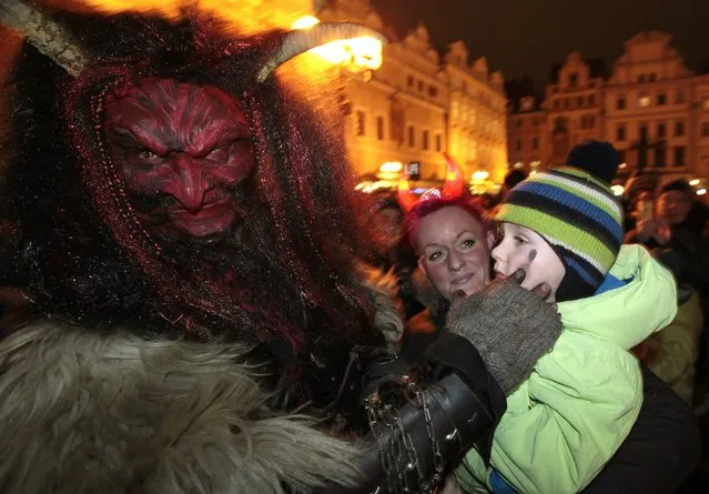 A reveller dressed as a devil strokes a child at the Old Town Square in Prague, on the eve of Saint Nicholas Day December 5, 2014. Revellers dressed as Saint Nicholas and a devil approached children on the streets as part of a tradition to determine if they had behaved well during the past year and depending on their answers, would receive presents, sweets or coal accordingly. (Photo by David W. Cerny/Reuters)