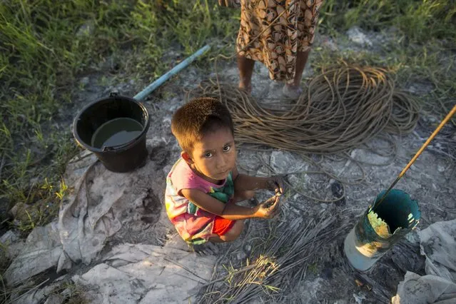 A child squats on the ground as her mother works to extract crude oil by hand on the seashore in Kyaukpyu township, Rakhine state, Myanmar October 5, 2015. (Photo by Soe Zeya Tun/Reuters)