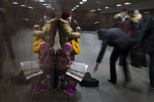 Ksenya, a street musician from a village in Kaluga region,  about 160 km. (100 miles) from Moscow, plays guitar to earn money in an underground subway with her daughter in Moscow, Russia, Wednesday, December 17, 2014. She earns about 3000 Rubles (about $ 46 USD) a day and works a few days a month to make ends meet. (Photo by Alexander Zemlianichenko/AP Photo)